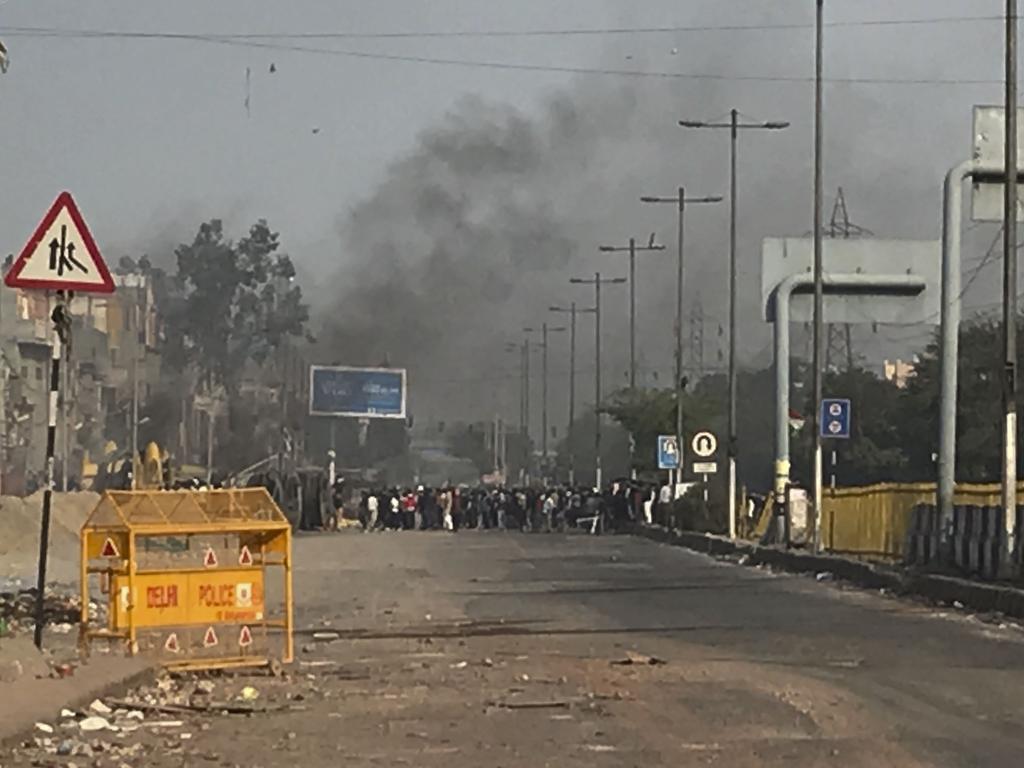 A mob throws stones at police as smoke rises from buildings set on fire following violence between two groups in New Delhi, India. Picture: AP