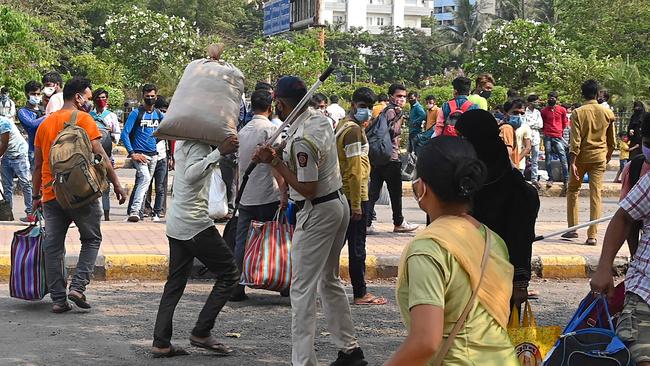 A Railway Police Force member wields a stick to control passengers arriving with their luggage outside Lokmanya Tilak Terminus railway complex to board a train back home ahead of the harvest season, in Mumbai amid rising COVID-19 cases. Picture: AFP