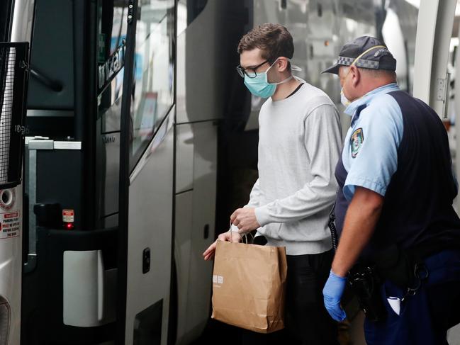 A member of the NSW Police Force escorts a returning overseas traveller onto a waiting bus at Sydney Airport on March 30. Picture: Getty Images