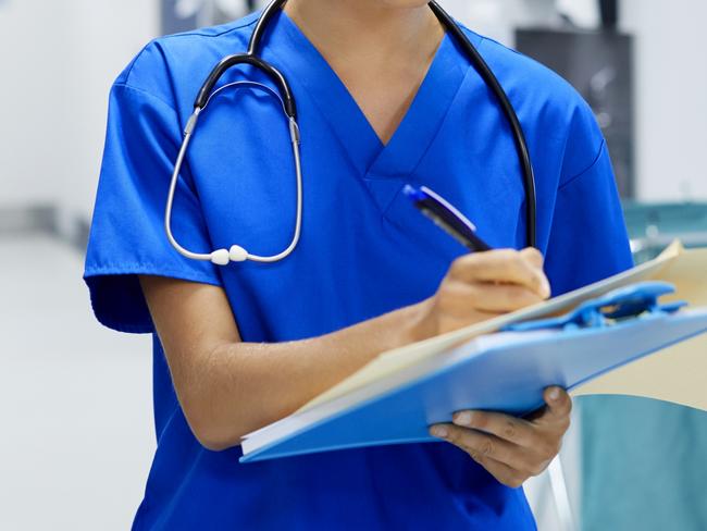 Confident female surgeon writing in file. Young medical professional is working in hospital corridor. She is wearing scrubs.