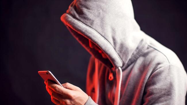 Man wearing hoody sweater with mobile phone in hands. Crime and hacking concept; scam generic.