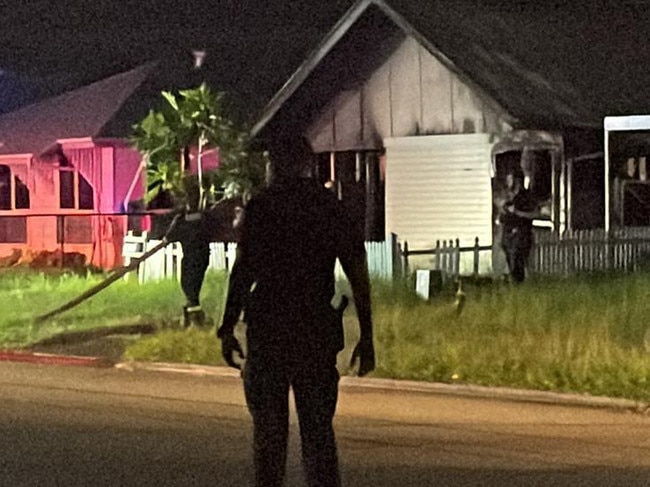 A police officer watches over the scene at a house fire in Ramsay St, Garbutt, which was under control before 9pm.