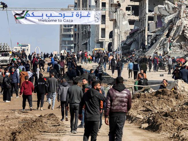 TOPSHOT - People gather by a banner welcoming people near the rubble of a collapsed building along Gaza's coastal al-Rashid Street for people to cross from the Israeli-blocked Netzarim corridor from the southern Gaza Strip into Gaza City on January 26, 2025. Israel said on January 25 it would block the return of displaced Palestinians to their homes in northern Gaza until Arbel Yehud, one of the hostages taken captive during the October 7, 2023 attacks, is released. Hamas sources said that Yehud was "alive and in good health", and would be "released as part of the third swap set for next Saturday", on February 1. (Photo by Omar AL-QATTAA / AFP)