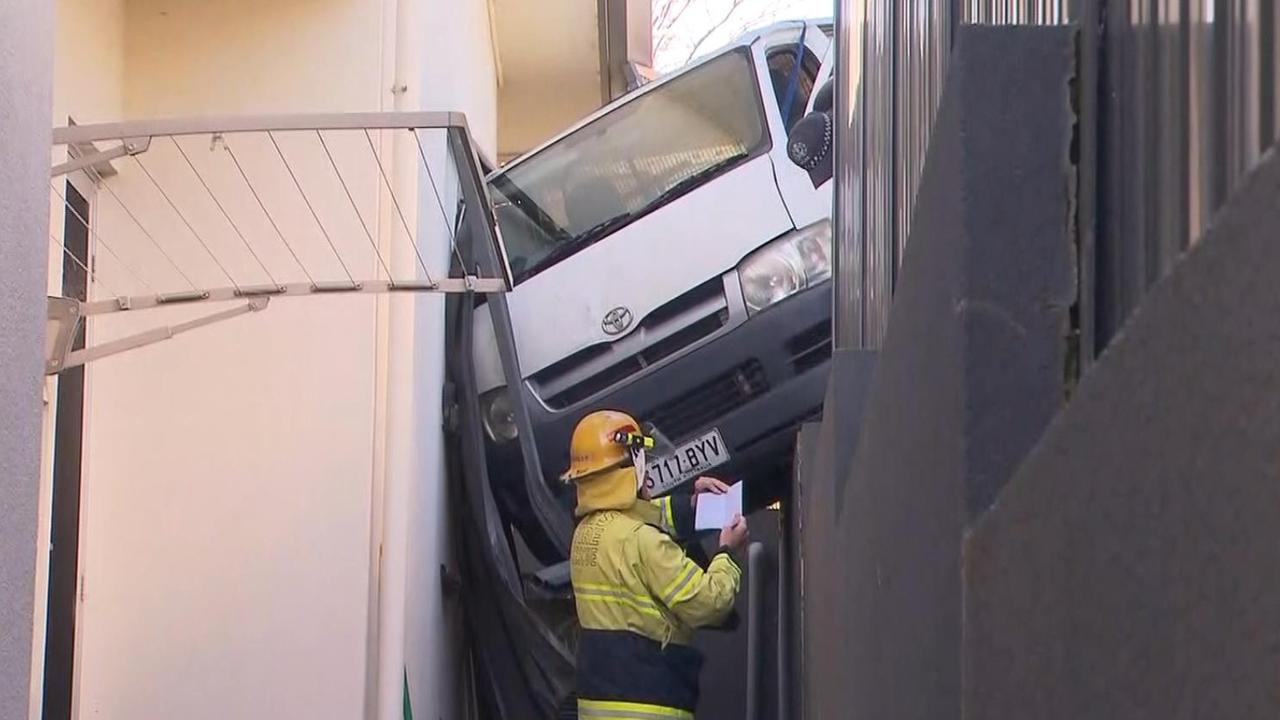 A courier driver has had a bad start to the day after his van went over a retaining wall and became wedged between a house and fence at Torrens Park. Picture: 7NEWS