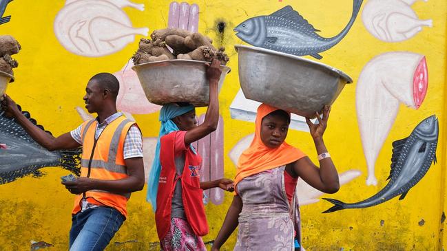 Two women take baskets to a market in Accra, Ghana. One carries a bundle of tubers, while the other appears to be carrying one of the painted fish on the wall behind her. Picture: Regula Tschumi