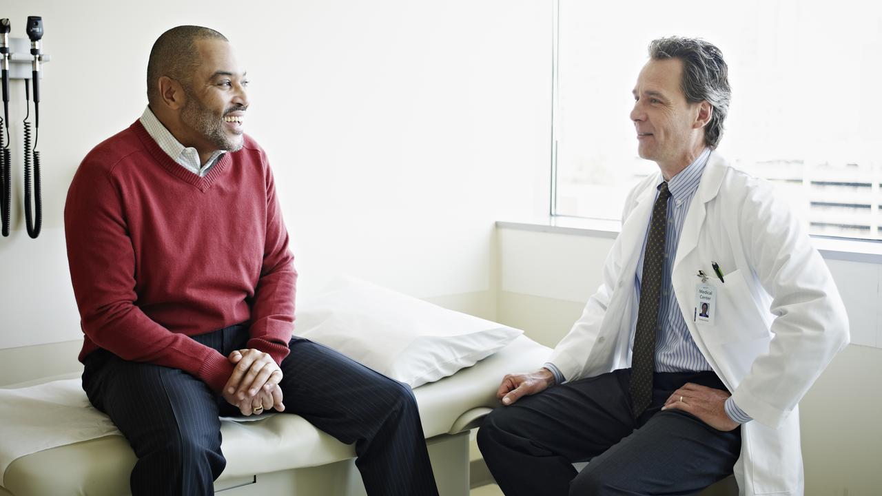 Mature male patient sitting on exam table in discussion with doctor in exam room