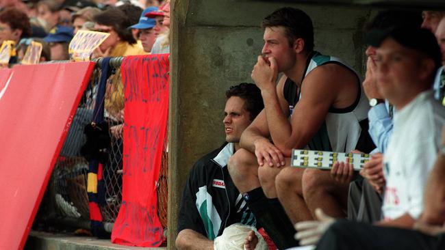 Gavin Wanganeen sits on Port’s interchange bench with injured right ankle ligaments, as Matthew Primus watches the game alongside.