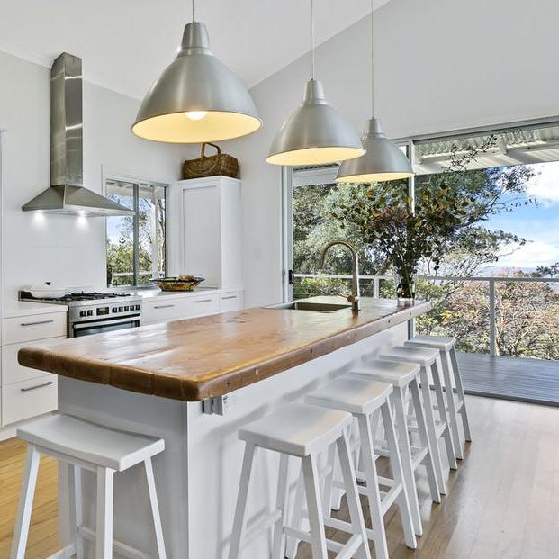 The all-white kitchen overlooks bushland.