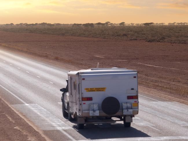 SOLO TRAVEL COLUMN - JANUARY .. for Louise Goldsbury story ..  An Australian Outback touring caravan on the road in the early morning near Eucla, on the Western/South Australia border. The markings on the road show it is a Flying Doctor landing strip.