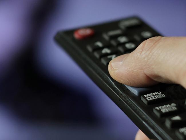 A hand with remote control and TV in the background