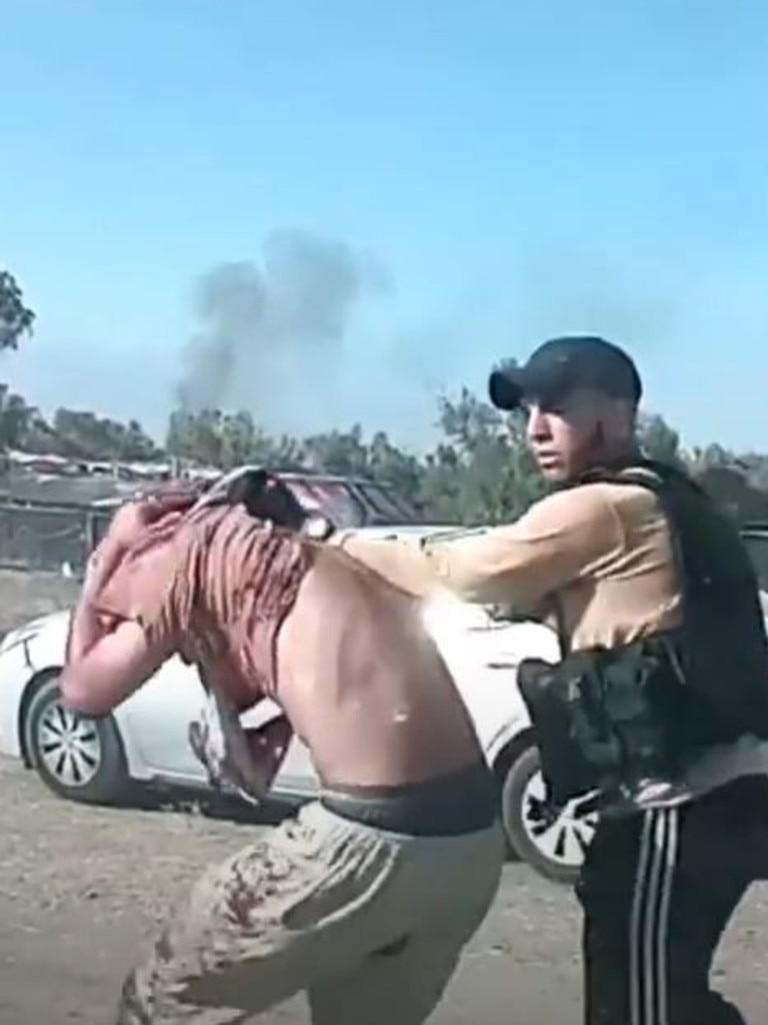 In one clip, a man is seen being marched at gunpoint by a Hamas militant. Blood is streaming from a gash in his arm and another man is lying motionless behind a car in the background. Picture: Supplied