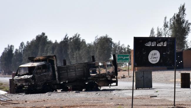 A burnt out vehicle next to a banner bearing the Islamic State group's flag in the village of Dibsiafnan on the western outskirts of the Islamist's Syrian bastion of Raqa. Picture: AFP Photo/George Ourfalian