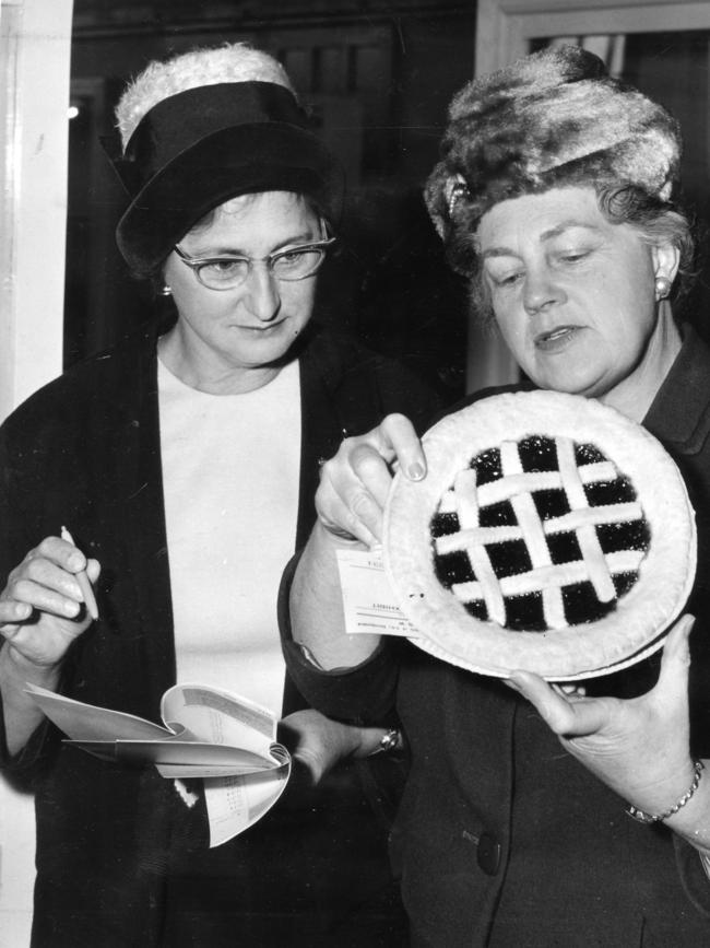 1964 — Steward Mrs. R. Shepperd looks on while judge Mrs. N. Matheson inspects a jam tart from the junior cookery entries in the Royal Show Handicraft Pavilion.