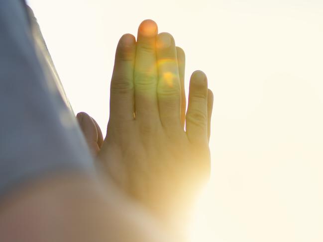 Hands of man praying at sunset