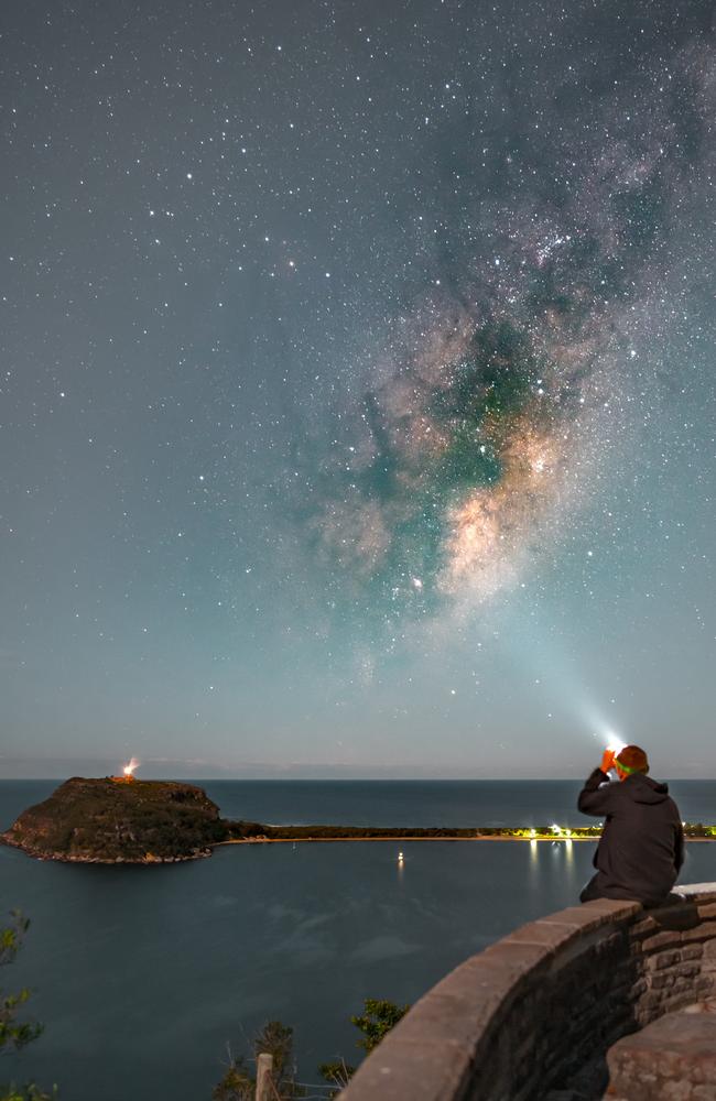 A man sitting at West Head lookout looking up to the Milky Way with Barrenjoey Headland in the background. Picture Greg Barber