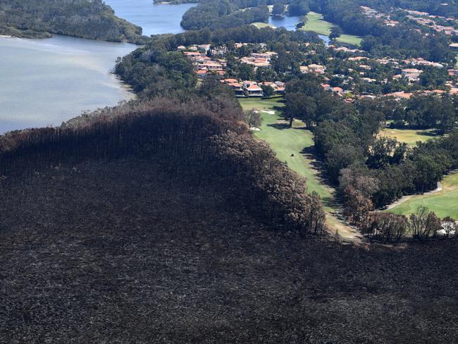 Golfers are seen on the green next to a bushfire-damaged area in Noosa Heads on the Sunshine Coast, Tuesday, September 10, 2019. About 70 blazes are still burning across Queensland, with 15,000 hectares scorched since the fire crisis began late last week. (AAP Image/Dan Peled) NO ARCHIVING