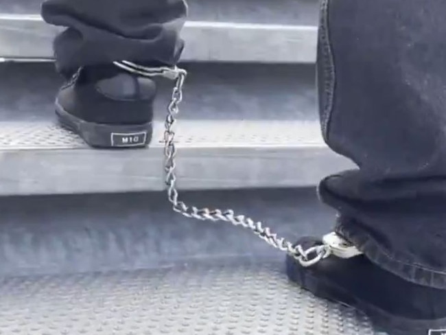 One shot shows a person with chains around their feet as they walk up the stairs to board the plane. Picture: X