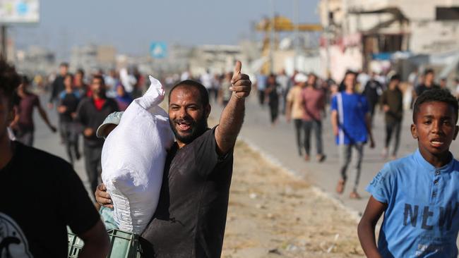 A man gestures with a thumbs up as he ferries a bag of food aid while others rush to get a share after people stormed a World Food Programme warehouse in Deir el-Balah. Picture: AFP.