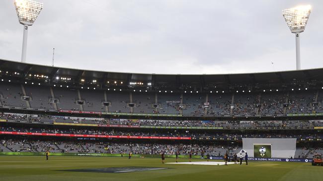 Lights are on as ground staff cover the pitch at the Melbourne Cricket Ground. Picture: AP.