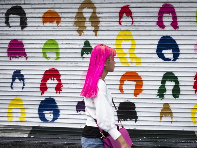 A woman with pink hair walks along Hollywood Boulevard past a colorful storefront shutter Wednesday, July 18, 2018, in Los Angeles. (AP Photo/Jae C. Hong)