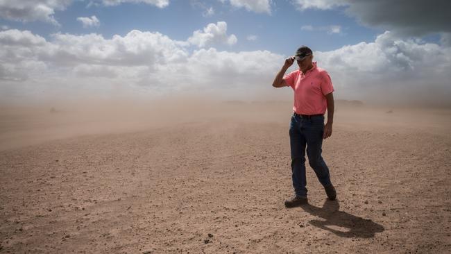 Dan Boland struggles to walk through a paddock as strong winds kick up a dust storm. Picture: Jake Nowakowski