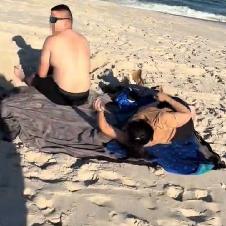 The pair are sitting on separate towels on the sand with a dog running around them. Picture: TikTok