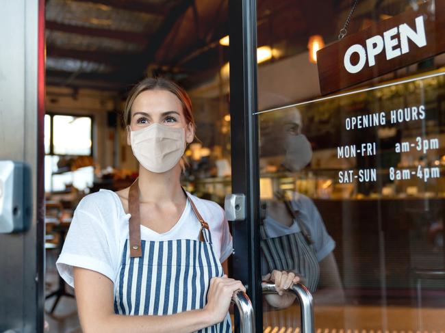 Happy business owner opening the door at a cafe wearing a facemask to avoid the spread of coronavirus ÃÂ¢Ãâ¬Ãâ reopening after COVID-19 concepts