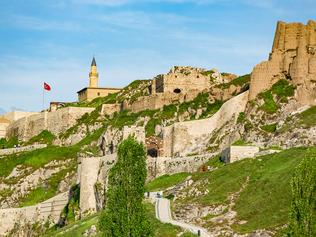 Van, Turkey - May 23, 2015: Tourists walking at castle road and castle and Turkish flag is flying near the minaret in Van Castle of Turkey at sunny day condition.