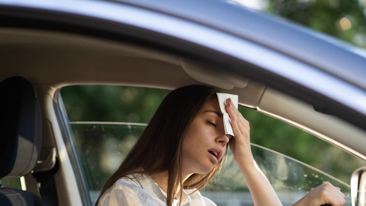 Girl driver being hot during heatwave in car, suffering from hot weather, has problem with a non-working air conditioner, wipes sweat from her forehead with tissue. Summer, heat concept.