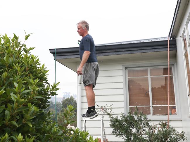 Geeveston resident Glen Ryan fills his neighbour’s gutters with water in preparation for the bushfire threat. Picture: NIKKI DAVIS-JONES