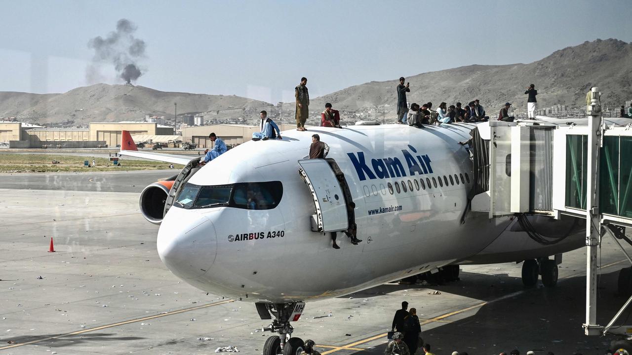 Afghan people climb atop a plane as they wait at the Kabul airport in Kabul.