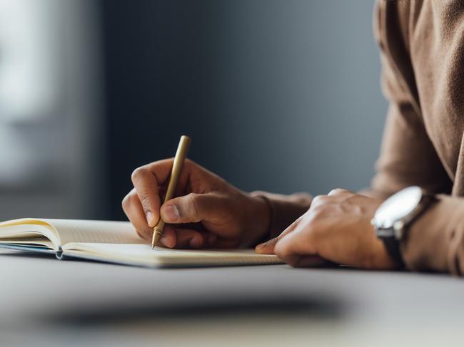 A close-up image of a man writing in a notebook with a pen at a desk, focusing on creativity and concentration.