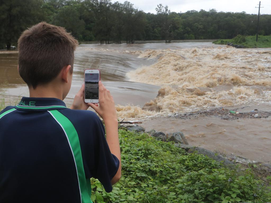 People gather to watch floodwaters in the Coomera River spill over the Oxenford Weir. Picture Glenn Hampson