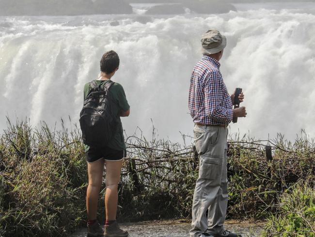 Victoria Falls, Zimbabwe, 19 September 2018. Two tourists at the Victoria Falls in Zimbabwe look across the gorge that receives millions of tons of water from the River Zambesi over the Victoria Falls in Zimbabwe. The waterfalls are divided between Zimbabwe and Zambia, with most of them being on the Zimbabwe side.