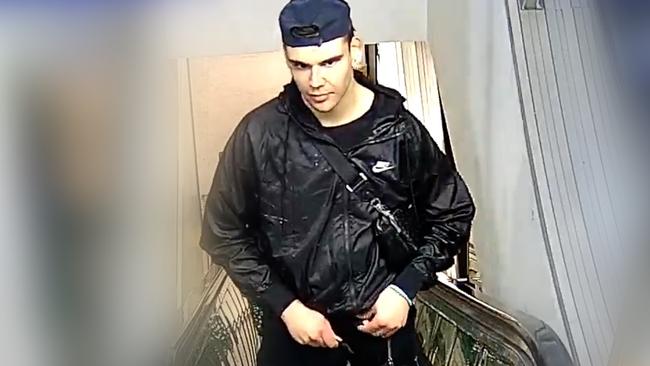 The man was wearing a backwards navy blue cap, black jacket, black pants, dark blue shoes and was carrying a black satchel bag.