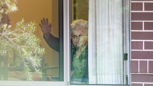 Patricia Shea (76) who is COVID-19 positive waves to her son who is outside the fence from the window of her accommodation at Newmarch House in May. Picture: Damian Shaw