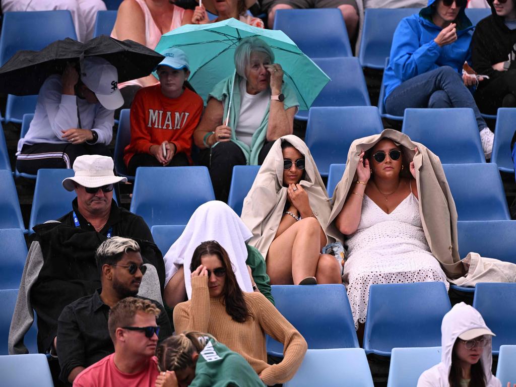 Fan shelter from the rain during a break in play at the Australian Open tennis tournament in Melbourne on Thursday. Picture: AFP