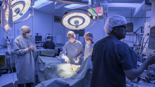 Surgical team performing operation in hospital operating room. Medical team with patient on operating table with surgical lights above. Istock