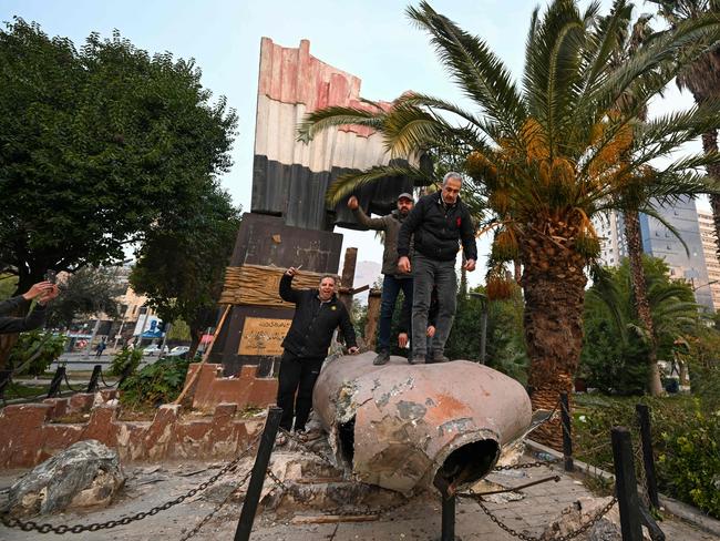 People stand atop a toppled statue of Syriaâs late president Hafez al-Assad in Damascus on December 8, 2024. Islamist-led rebels declared that they have taken Damascus in a lightning offensive on on December 8, sending President Bashar al-Assad fleeing and ending five decades of Baath rule in Syria. (Photo by LOUAI BESHARA / AFP)