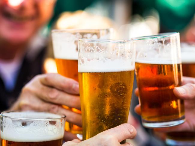 Close up color image depicting a group of people celebrating with a toast. The people cheers their glasses of beer (pints of beer) together in a gesture of celebration, togetherness and happiness. The people are defocused in the background, while focus is on the glasses of beer in the foreground. Room for copy space.