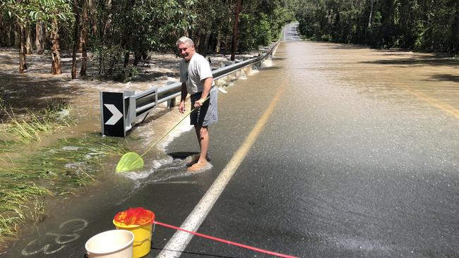 Carbrook resident David Venn making use of the flood waters to catch tiny native fish on the usually busy Beenleigh-Redland Bay Rd at Carbrook. WATCH THE VIDEO OF THE CASCADING WATERS PHOTO: JUDITH KERR