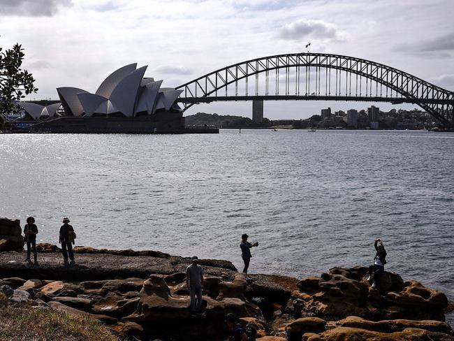 Tourists stand on rocks as they take photographs in front of the Sydney Opera House and Sydney Harbour Bridge on a spring day on November 13, 2023. (Photo by DAVID GRAY / AFP)