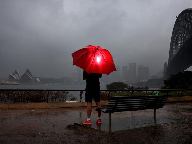 Heavy rains continue to drench Sydney, much to the relief of fire fighters who have battled bushfires across the state for months. A tourist holds an umbrella while looking out over a grey Sydney Harbour. Picture: Toby Zerna