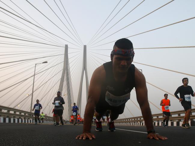 A participant does push ups as other runners compete along the Bandra-Worli sea link over the Arabian Sea during the Mumbai Marathon in Mumbai, India, Sunday, Jan. 20, 2019. Thousands of the city's residents alongside athletes took part in the marathon. (AP Photo/Rafiq Maqbool)