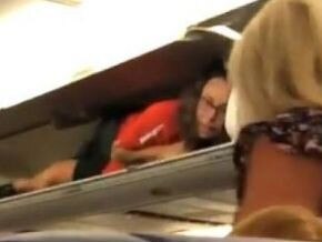 The air host was filmed hiding in the overheard luggage compartment.