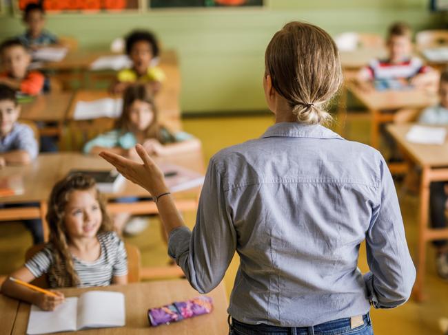 Back view of a female teacher teaching large group of elementary students in the classroom.