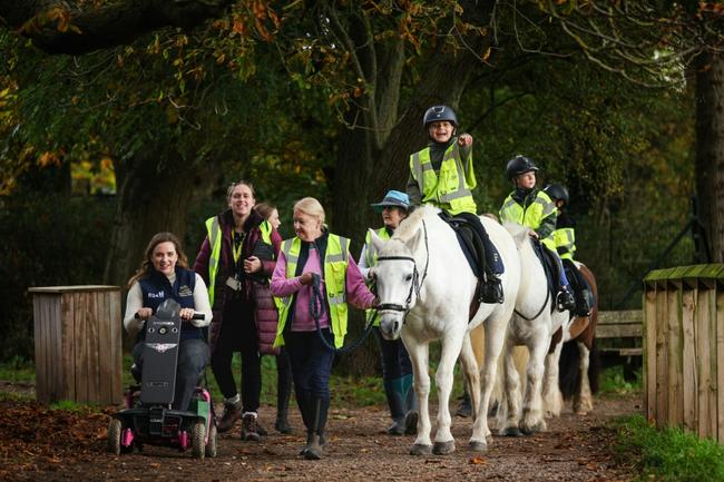 British Paralympian equestrian rider Natasha Baker (L) drives her mobility scooter alongside students from Clarendon Primary School and volunteers as they set off on a horse ride from Park Lane Stables RDA in Teddington, southwest London