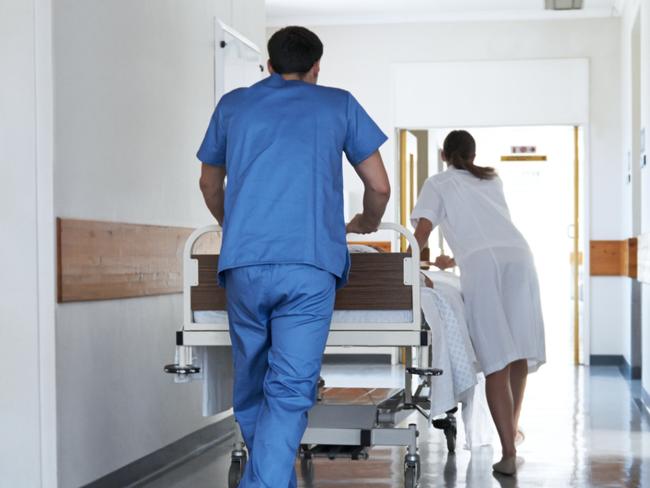 Rearview shot of hospital staff wheeling a patient in a gurney down a corridor