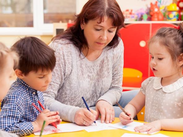 RendezView. Kindergarten teacher, beautiful, mature caucasian woman, brown hair, teaches pupils drawing. Two little girls and a boy. (Pic: iStock)