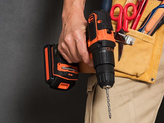 Close up of handyman holding a drill machine with tool belt around waist. Detail of artisan hand holding electric drill with tools isolated over grey background. Closeup hand of bricklayer holding carpentry accessories.